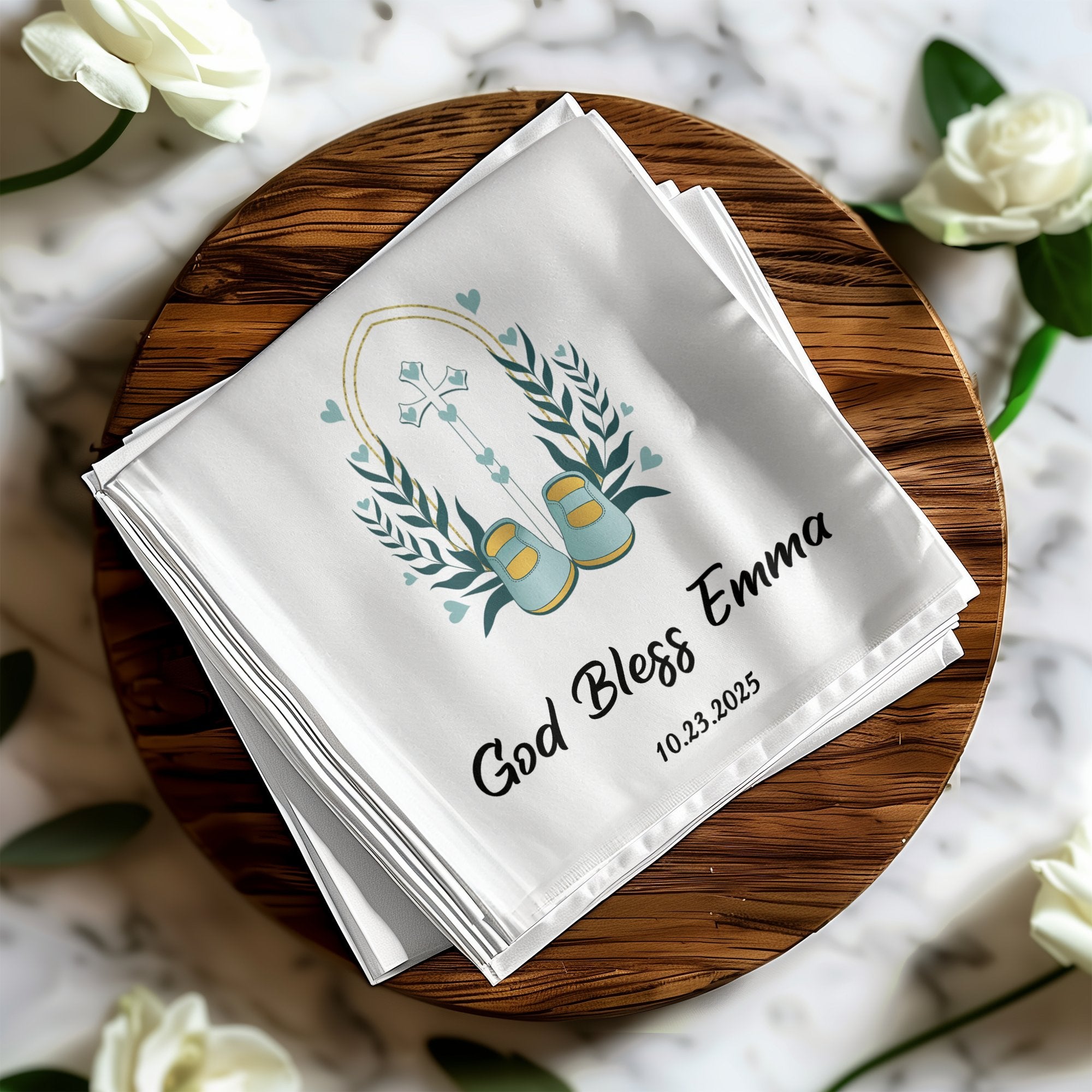 White handkerchief with cross, baby shoes, and "God Bless Emma 10.23.2025".