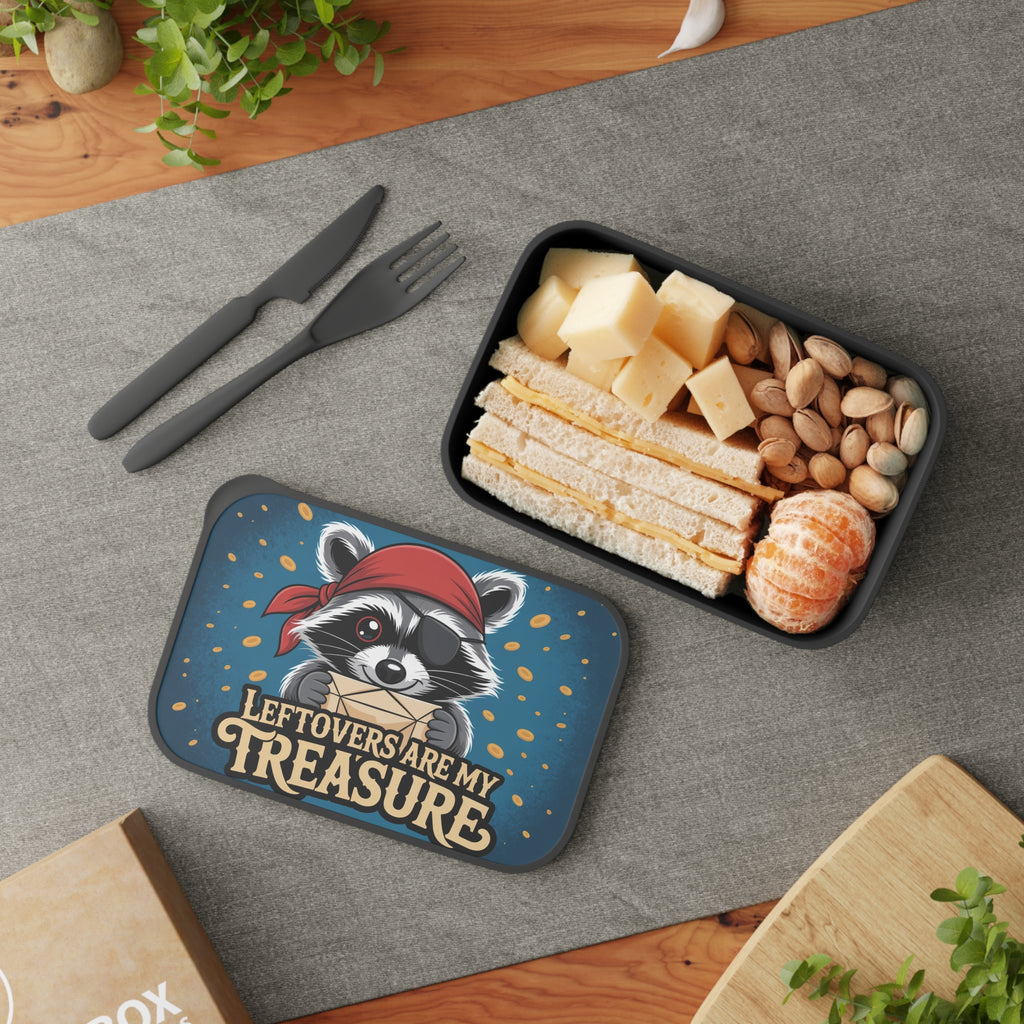 Lunchbox with raccoon wearing eye patch, sandwich, cheese, and nuts.