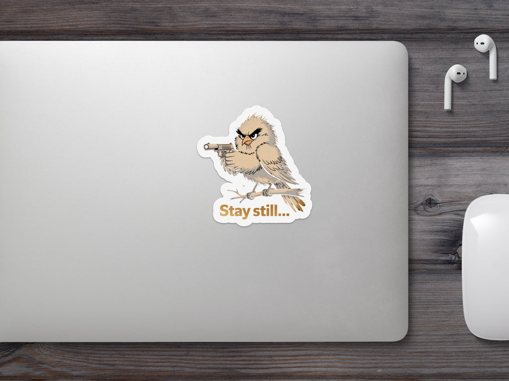 Bird with gun sticker on laptop, reads "Stay still..."