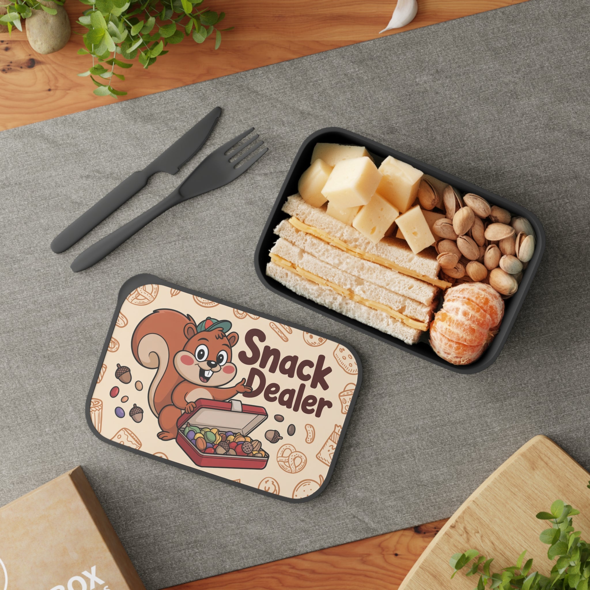 Black lunchbox with a smiling squirrel and snacks, containing sandwiches, cheese, and tangerines.