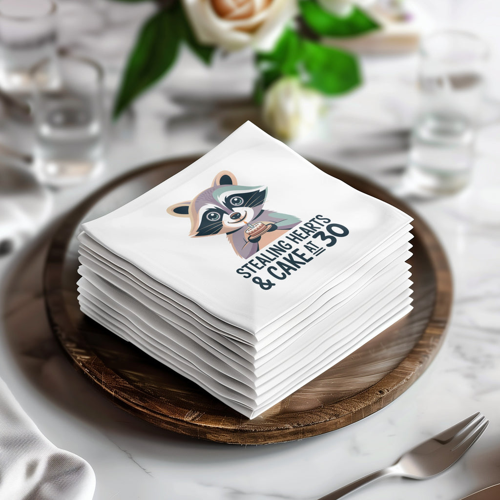 Stack of white napkins with a raccoon holding hearts and cake, reading "Stealing hearts & cake at 30".