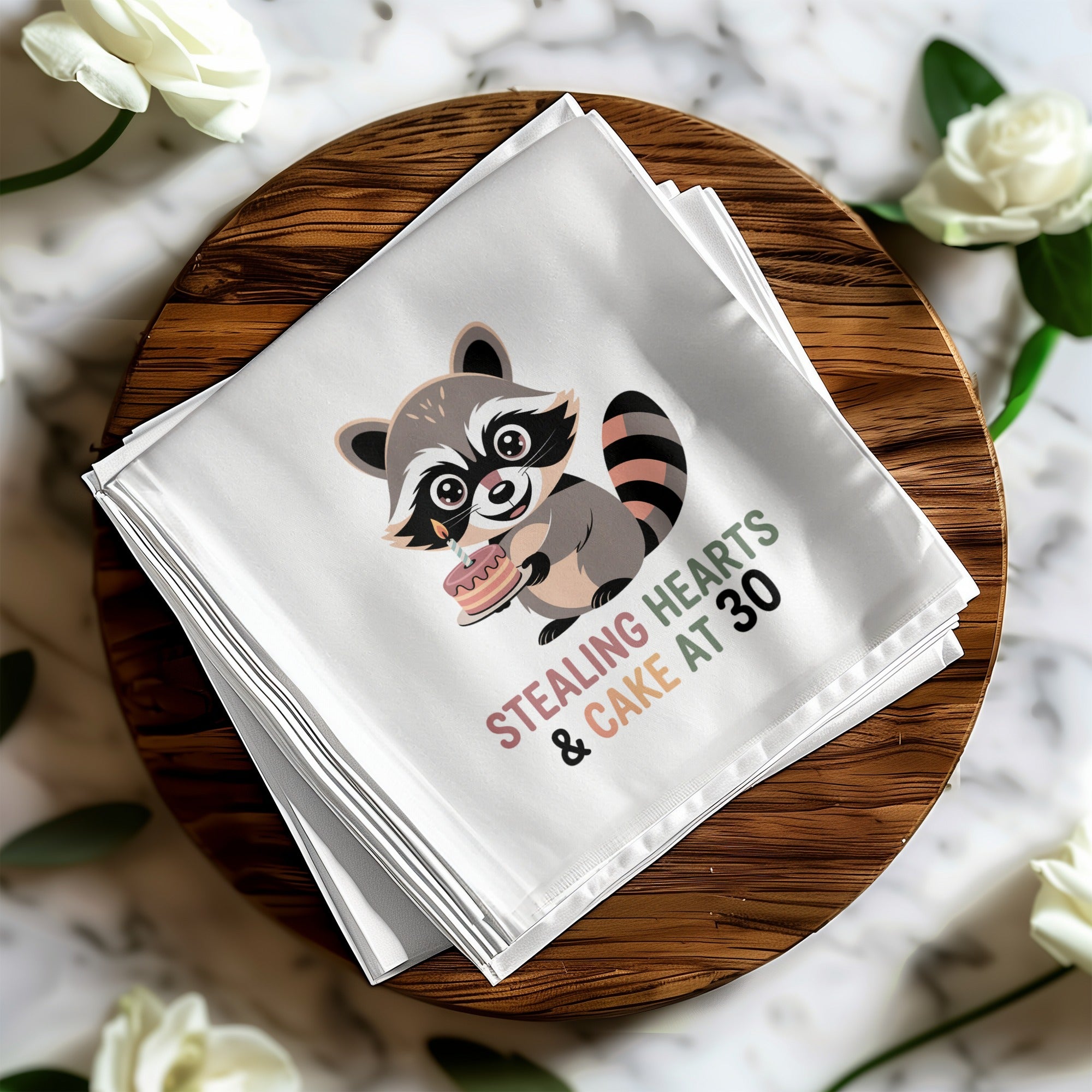 Cloth napkin with raccoon holding cake and text "Stealing Hearts & Cake at 30".