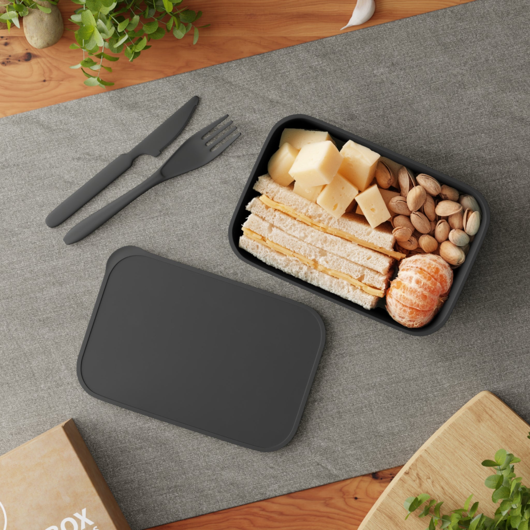 Lunchbox with sandwich, cheese, nuts, and tangerines on a gray mat.