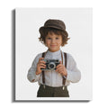 Young boy in suspenders and hat holding vintage camera.