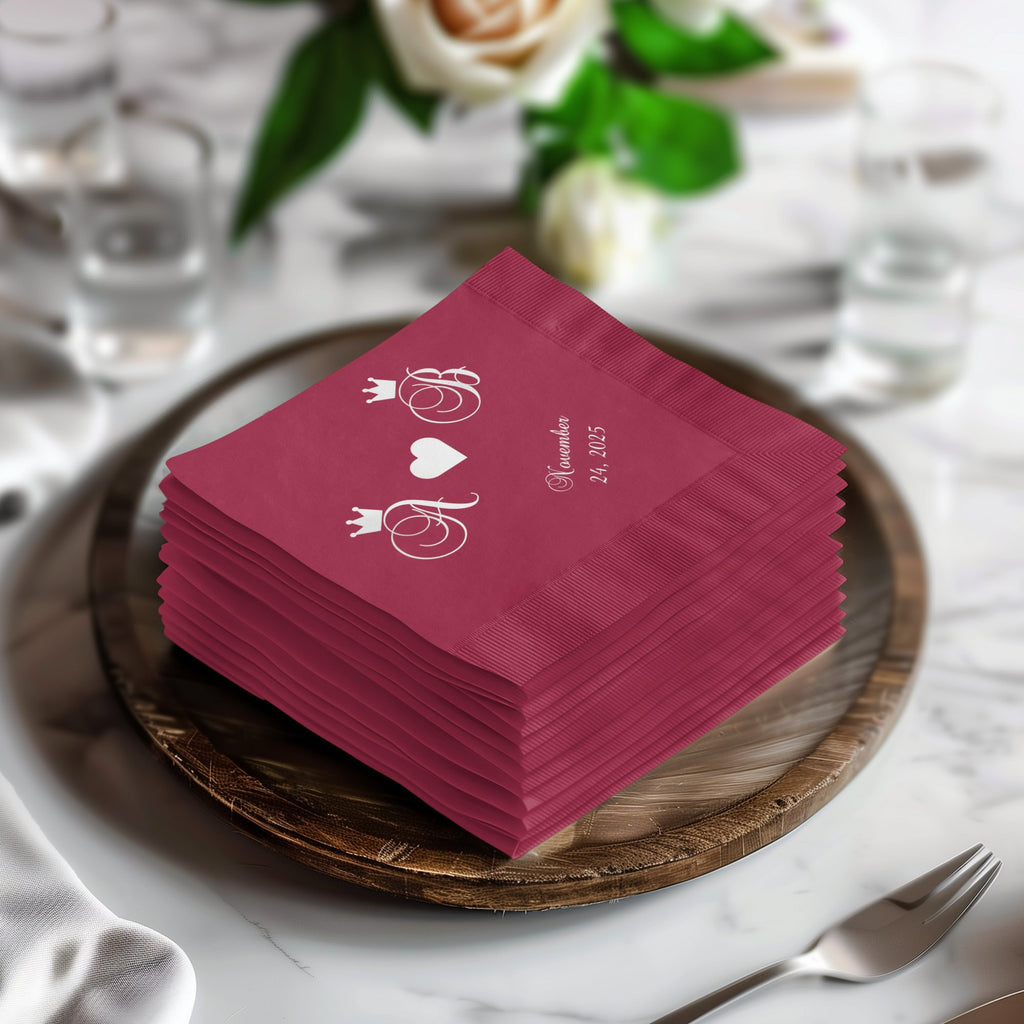 Burgundy wedding napkins stacked on a wooden plate with initials and date.