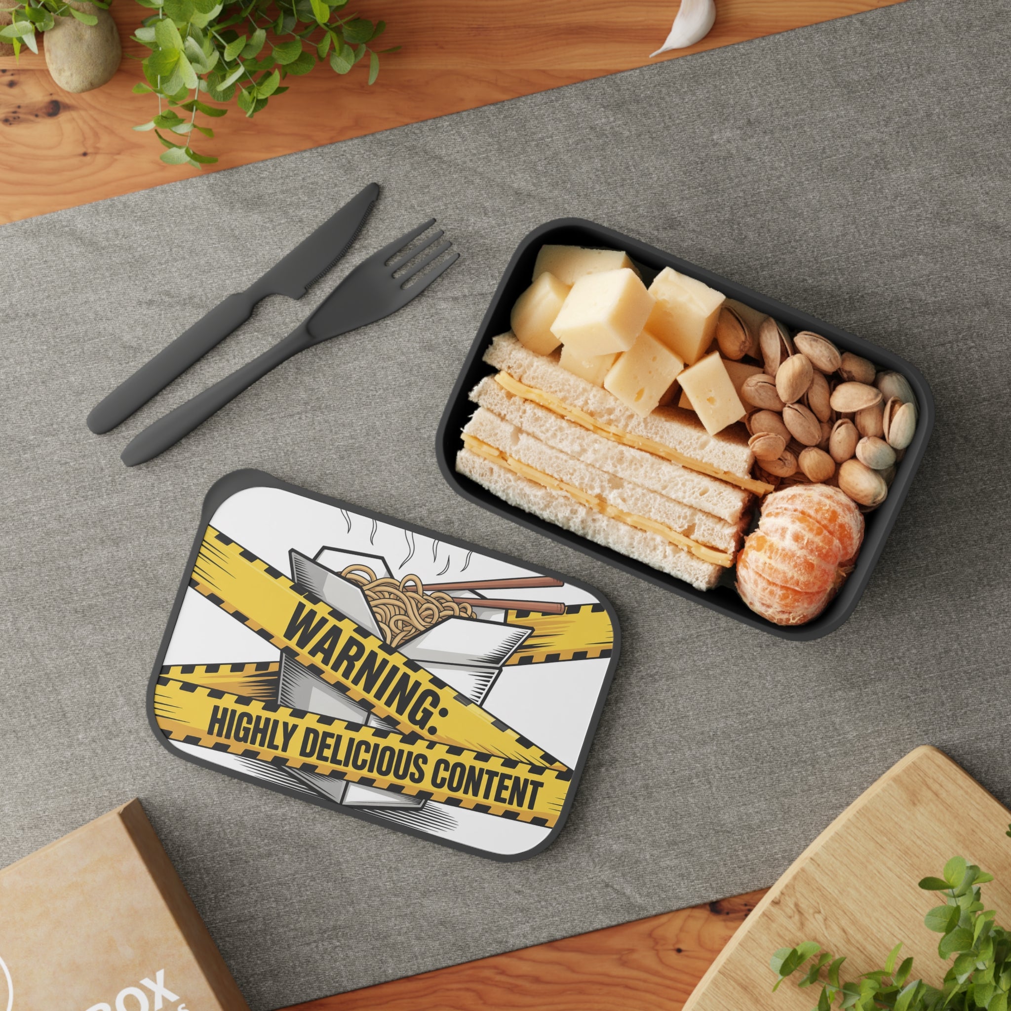 Bento box with sandwich, cheese, pistachios, and mandarins, lid reads "Warning: Highly Delicious Content."