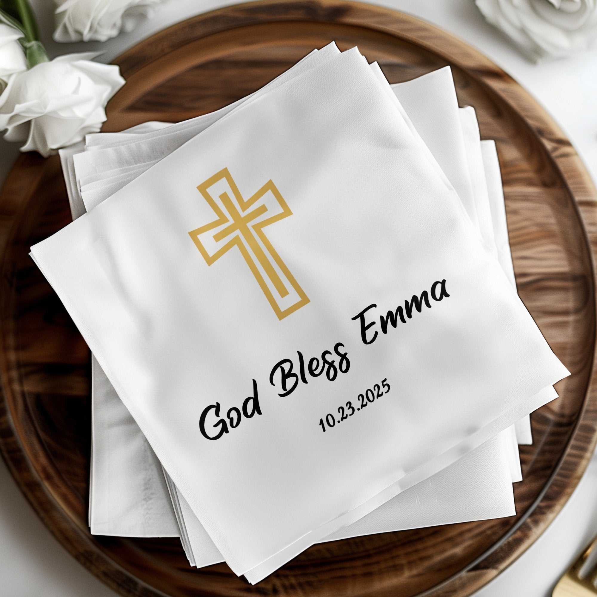 White napkin with gold cross and "God Bless Emma 10.23.2025" text.