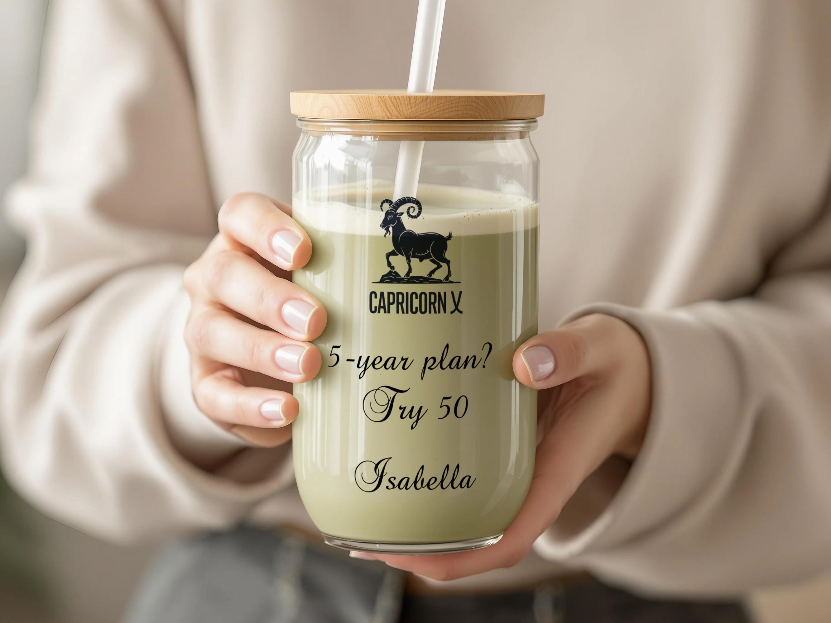 Glass tumbler with wooden lid, straw, and Capricorn zodiac sign with text.