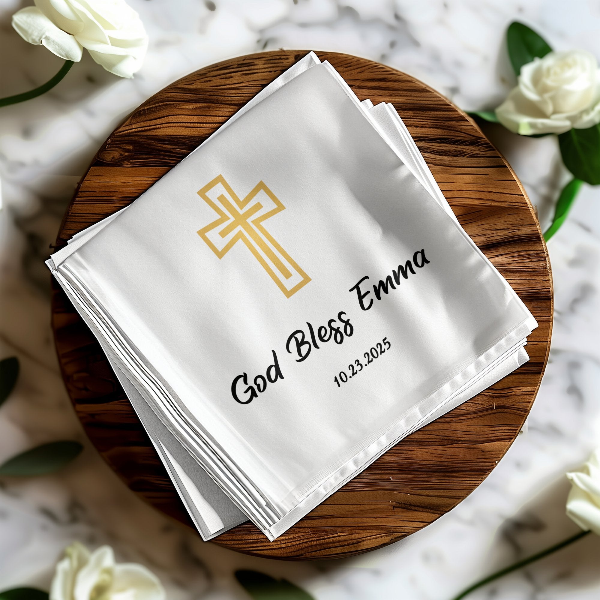 White cloth napkin with gold cross, "God Bless Emma," and date.