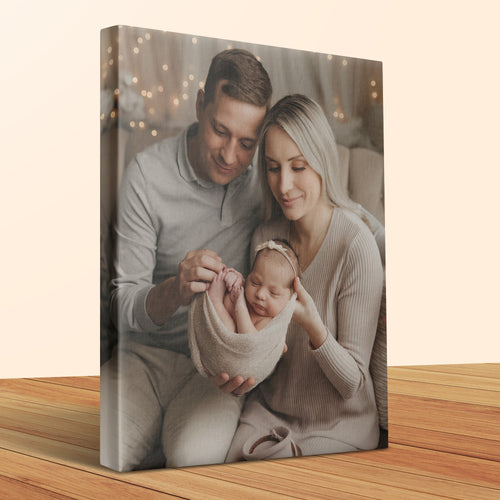Parents hold their newborn baby, wrapped in a light blanket.