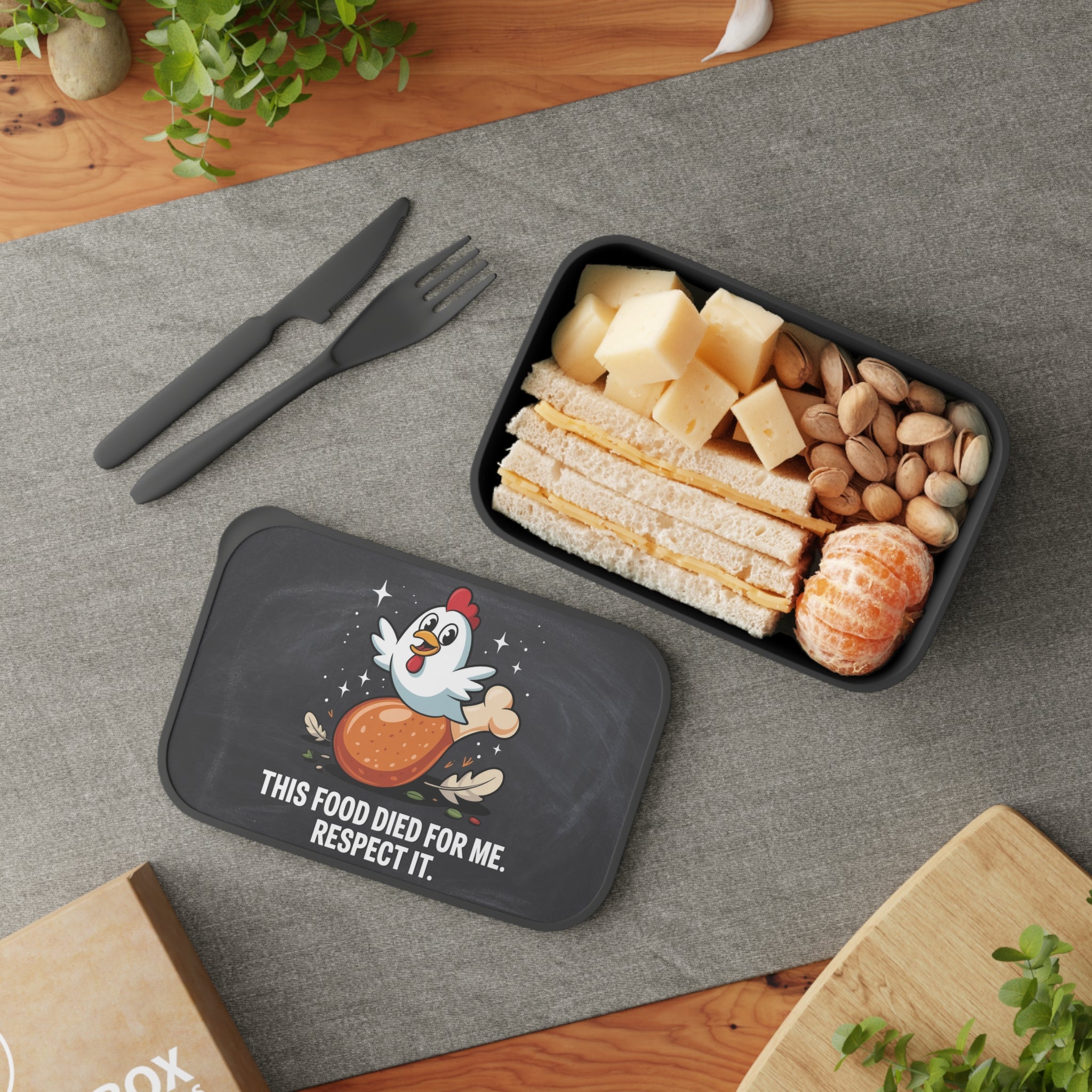 Lunchbox with chicken graphic and text, containing a sandwich, cheese, and nuts.