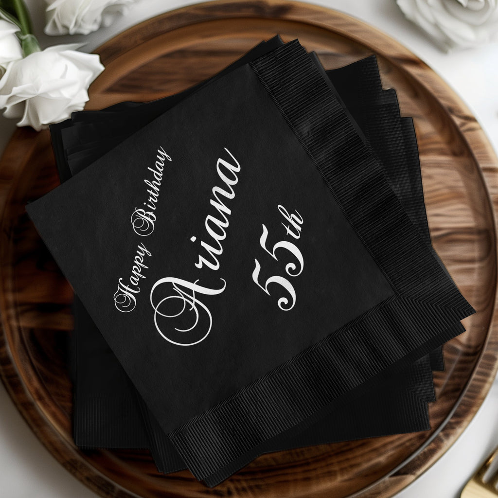 Black cocktail napkins with "Happy Birthday Ariana 55th" printed in white script.