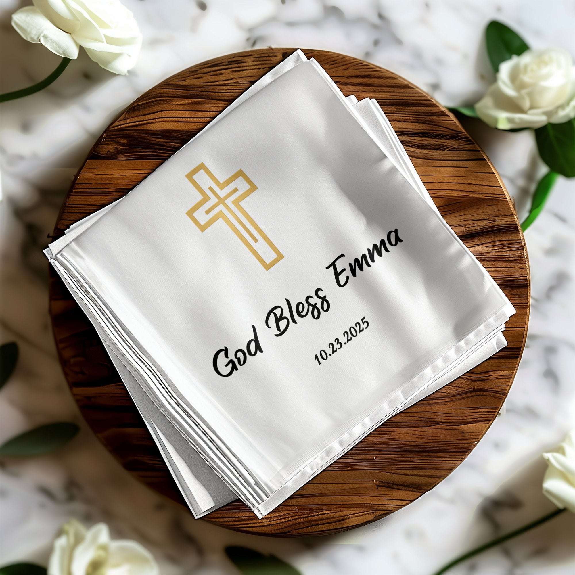 White cloth napkin with gold cross, "God Bless Emma", and date 10.23.2025.