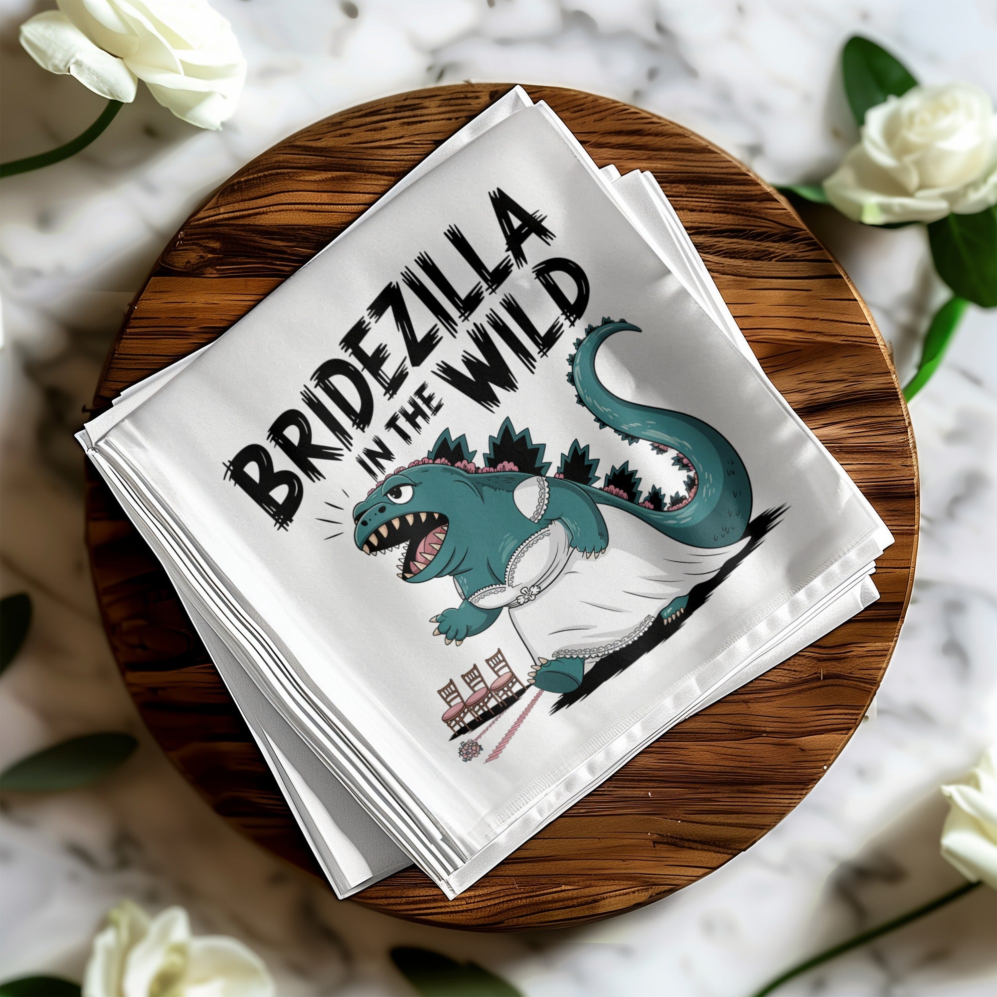 White napkin with "BRIDEZILLA IN THE WILD" text and illustration of a Godzilla-like creature in a wedding dress.