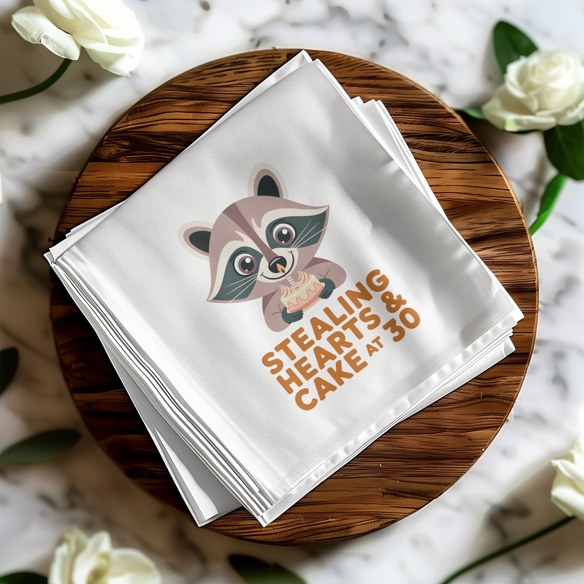 White napkin with a raccoon holding a heart-shaped cake and text "stealing hearts at 30".