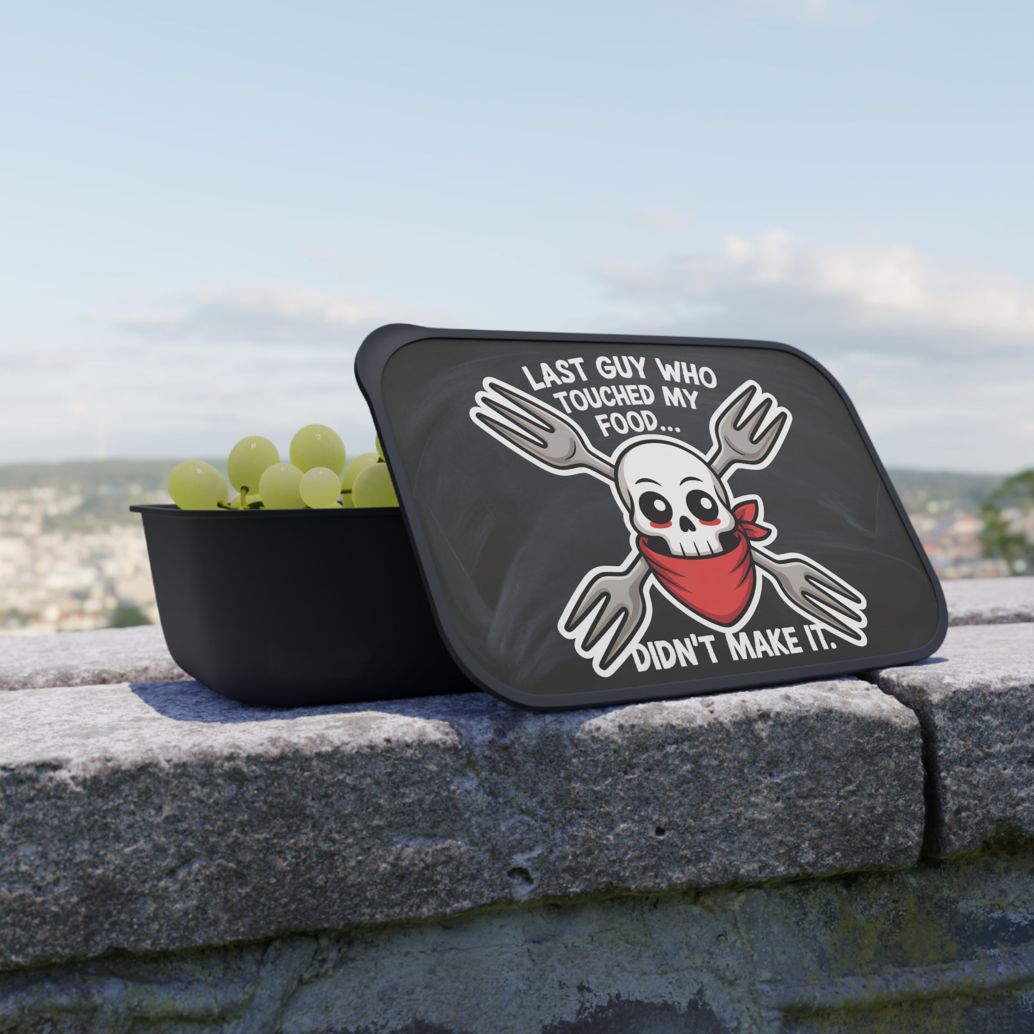 Black bowl with grapes and a lid featuring a skull with crossed forks and text.