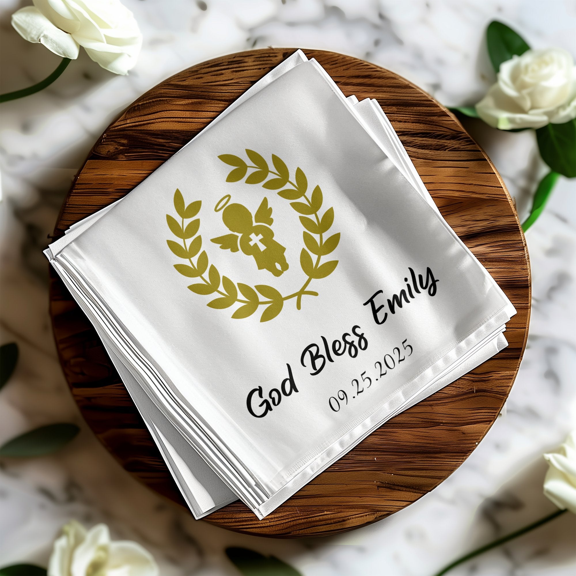 White folded napkin with gold angel, laurel wreath, "God Bless Emily," and date.