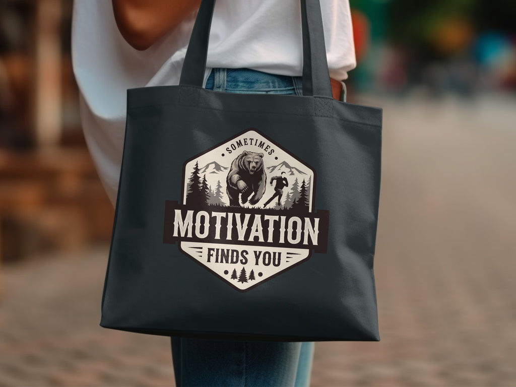 Dark grey tote bag with "Motivation Finds You" bear and runner graphic.