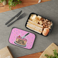 Pink lunchbox with a cake and knife graphic, next to a meal.
