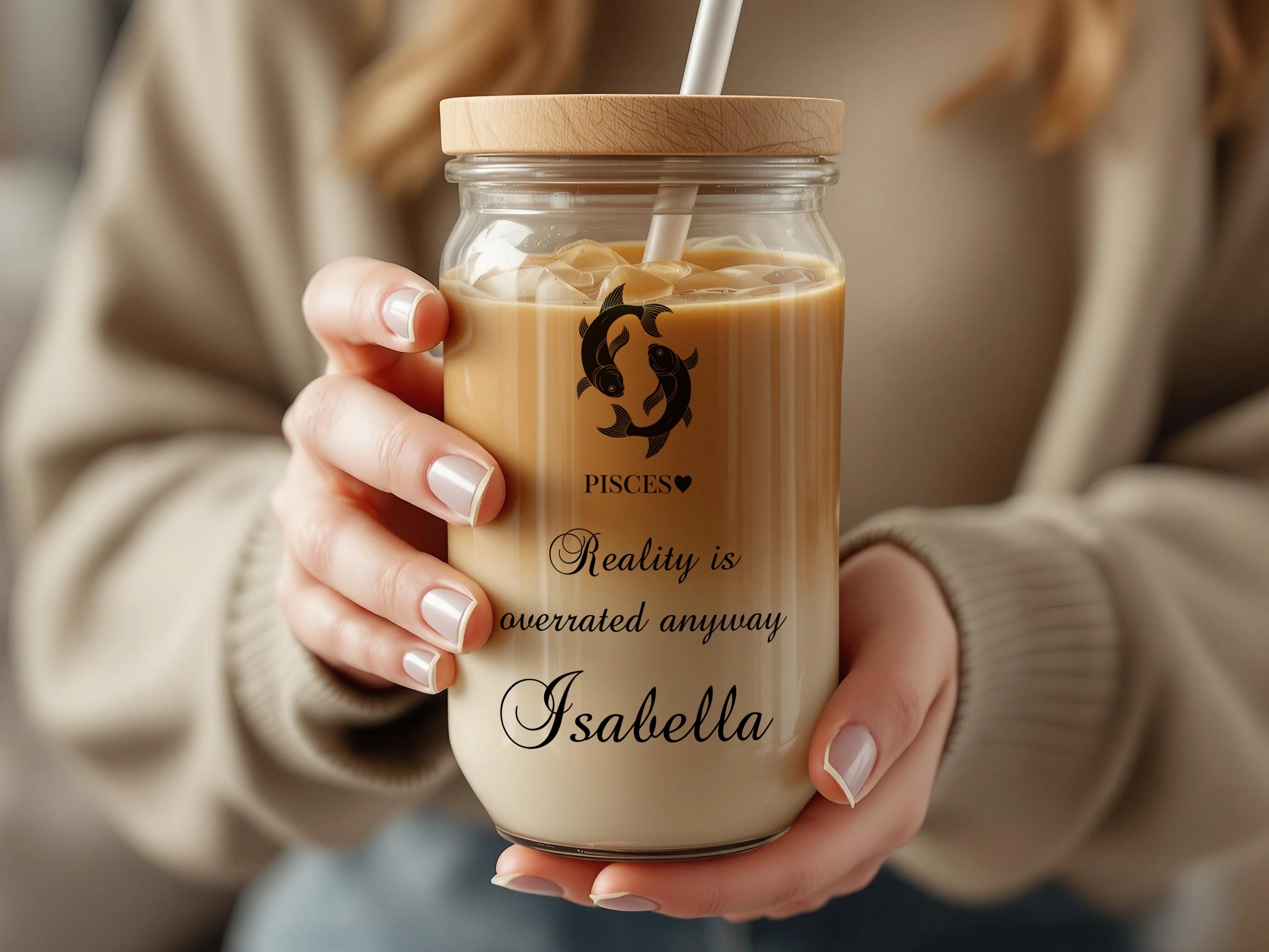 Pisces zodiac symbol and quote on glass tumbler with lid and straw, held by hands.