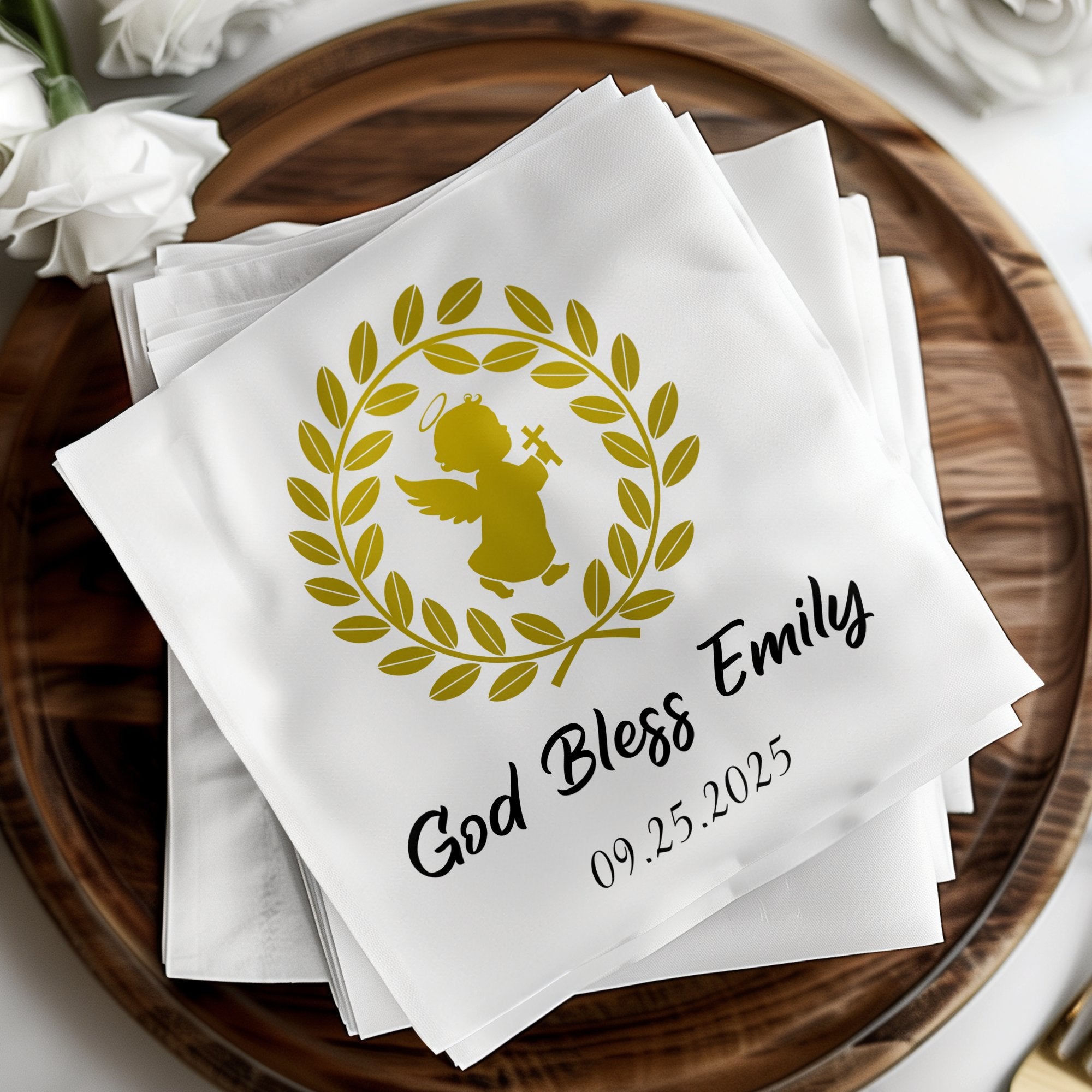White napkins with "God Bless Emily" and a date, adorned with a golden angel and laurel wreath.