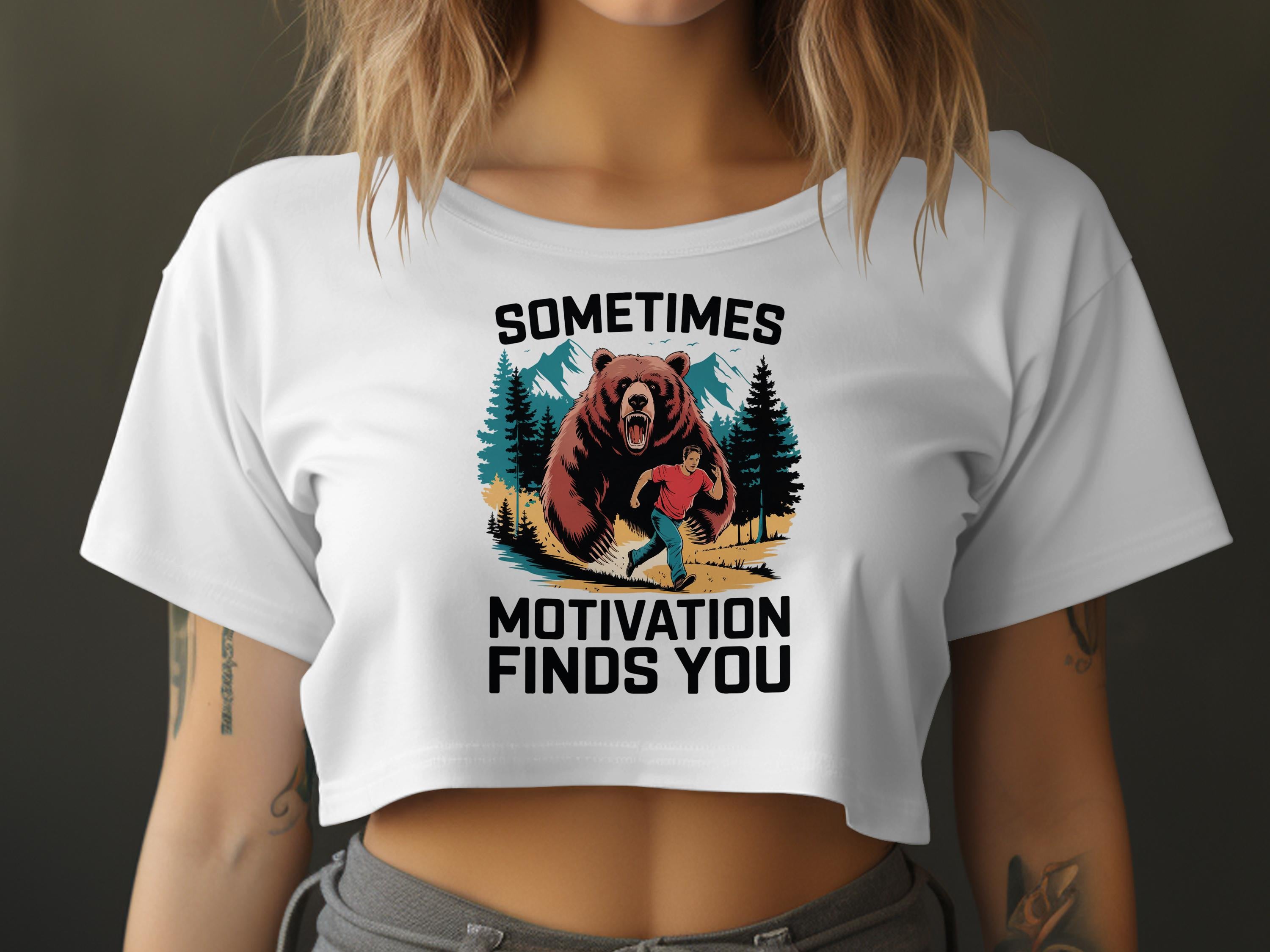 White cropped t-shirt with graphic of a man running from a bear and text "SOMETIMES MOTIVATION FINDS YOU".