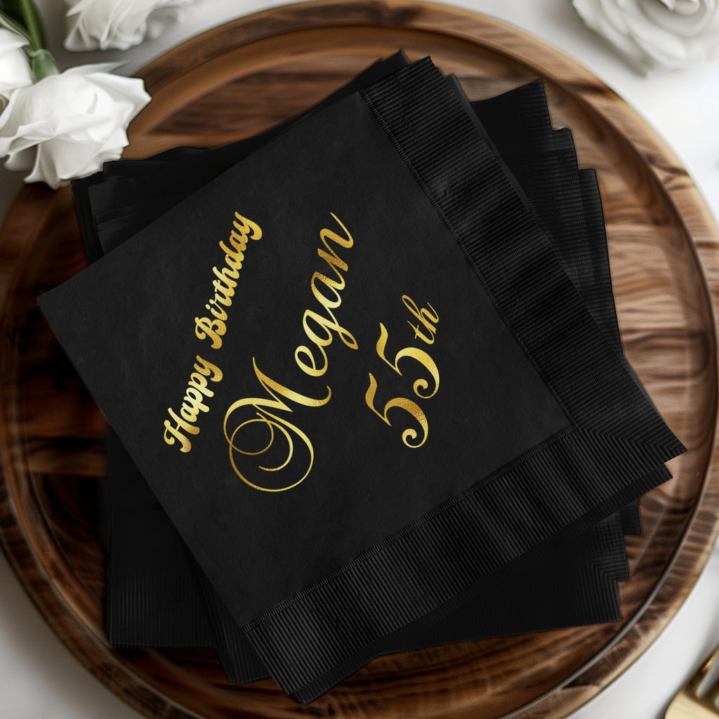 Black napkins with "Happy Birthday Megan 55th" in gold lettering.