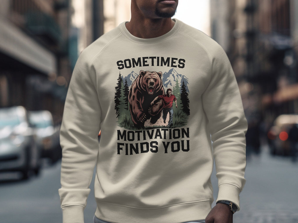 Cream sweatshirt with graphic of man running from a bear and text "Sometimes Motivation Finds You".