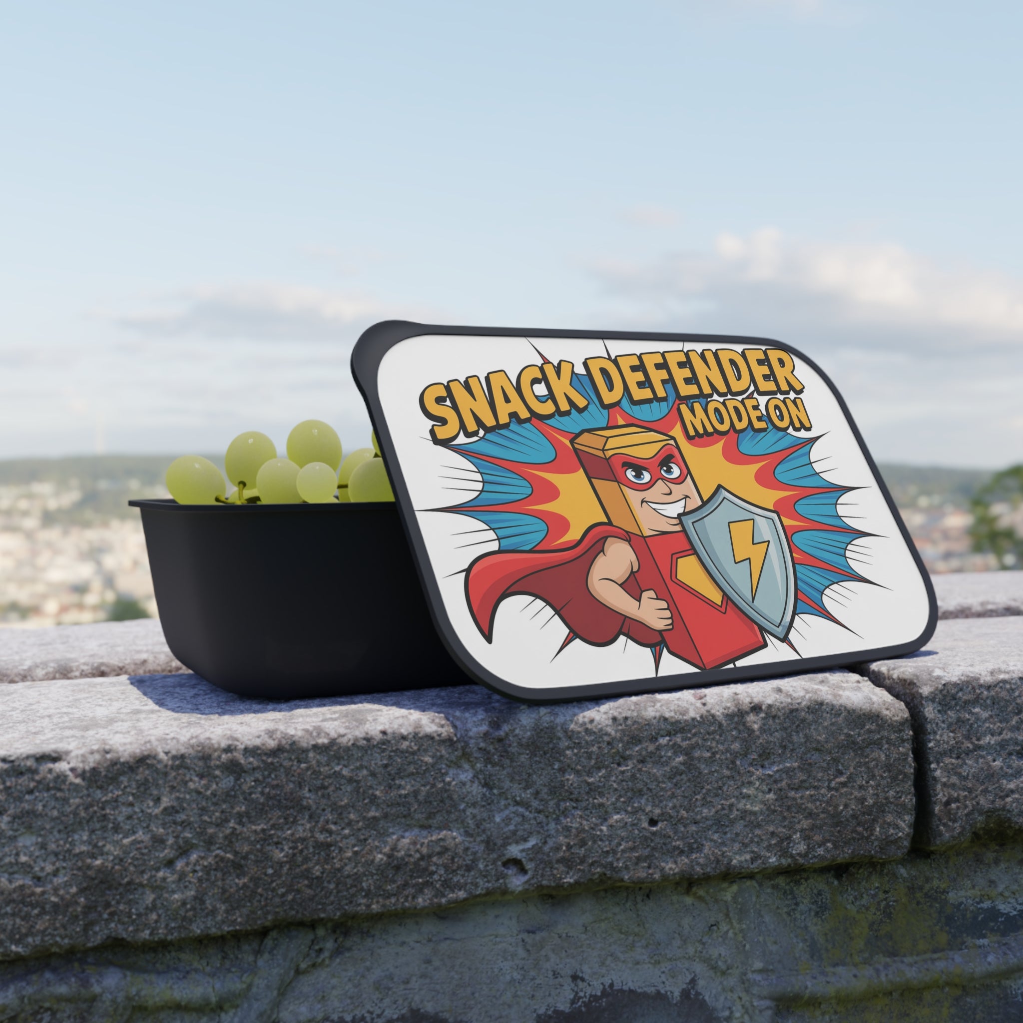 Black snack container with "Snack Defender" logo and green grapes.