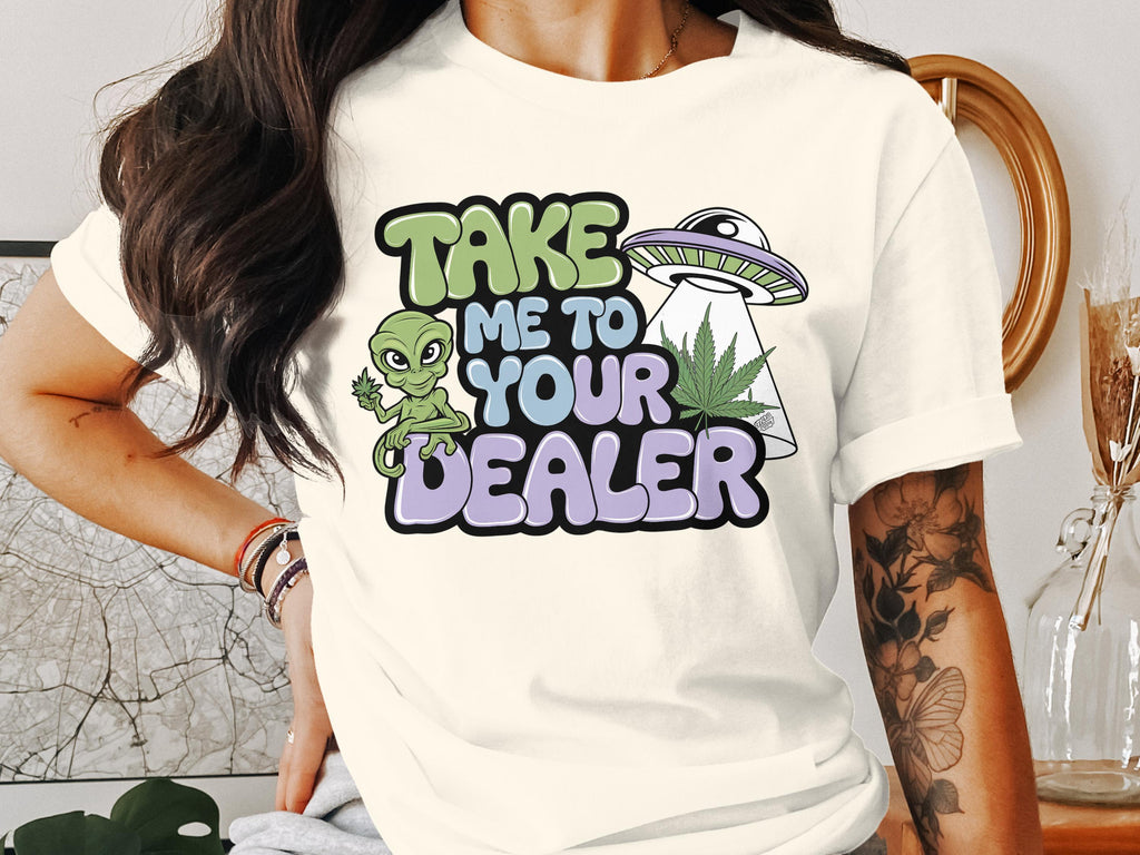 T-shirt graphic with alien, UFO, and marijuana leaf, reading "Take me to your dealer".