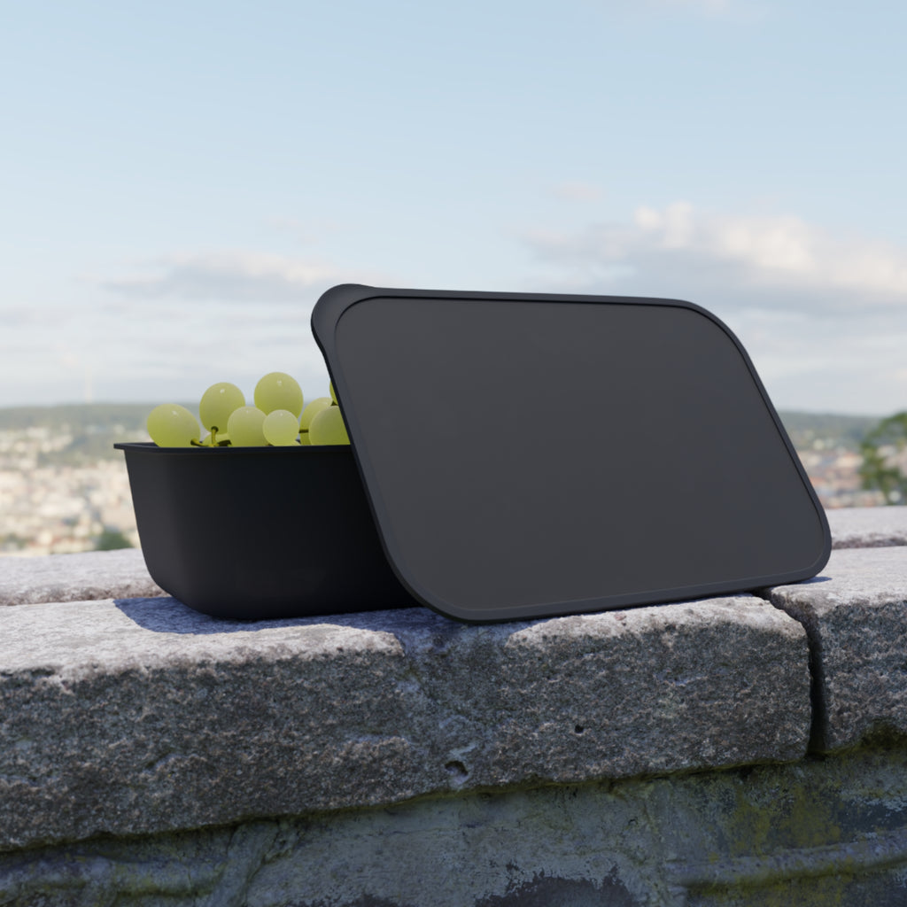 Black food container with lid open, filled with green grapes on a stone wall.