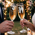 Two champagne flutes clink, etched with bride and groom figures and text.