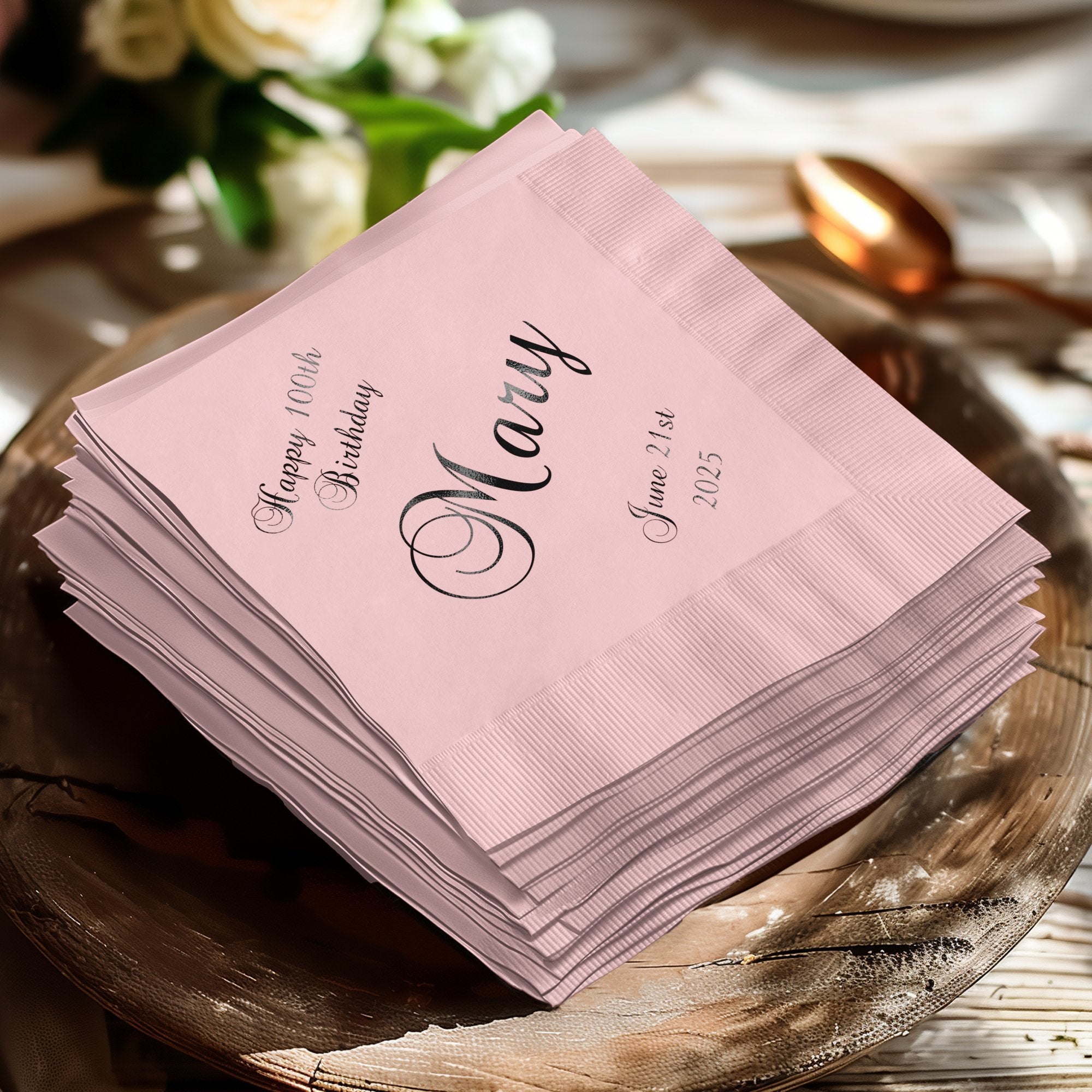 Pale pink cocktail napkins stacked, "Happy 100th Birthday Mary June 21st 2025."