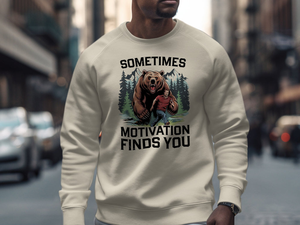 Cream sweatshirt with bear and man graphic and "Sometimes Motivation Finds You" text.
