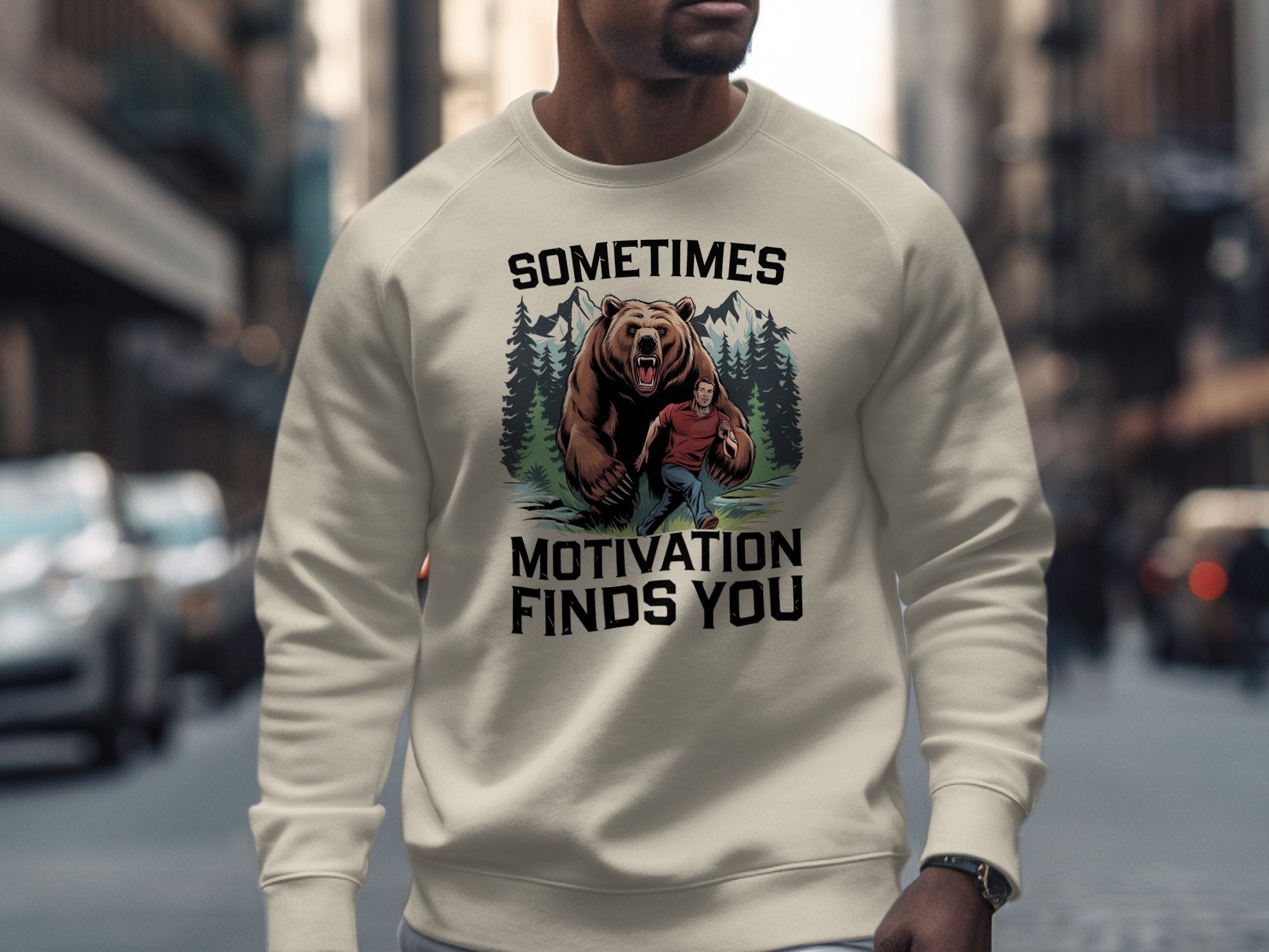 Cream sweatshirt with bear and man graphic and "Sometimes Motivation Finds You" text.