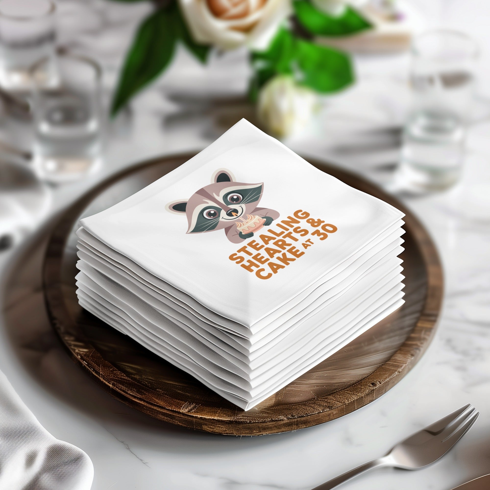 Stack of white napkins with raccoon illustration and "Stealing Hearts & Cake at 30" text.