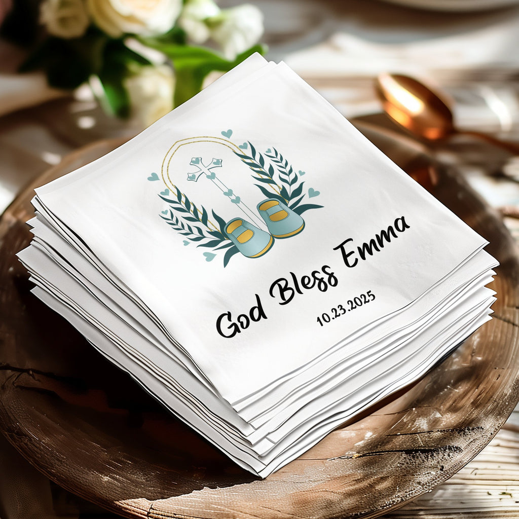 White napkin with "God Bless Emma" and date, decorated with a wreath and baby shoes.