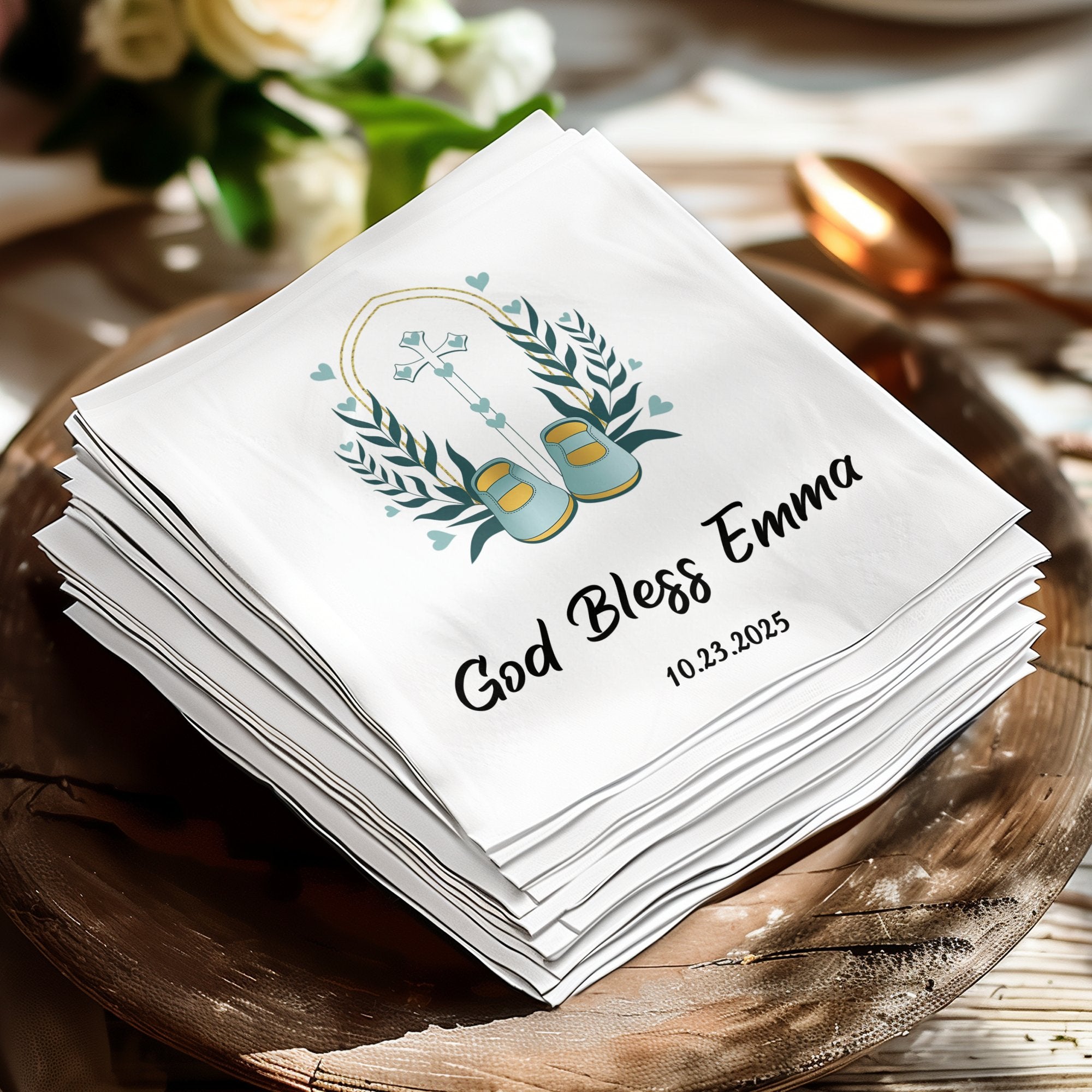 White napkin with "God Bless Emma" and date, decorated with a wreath and baby shoes.