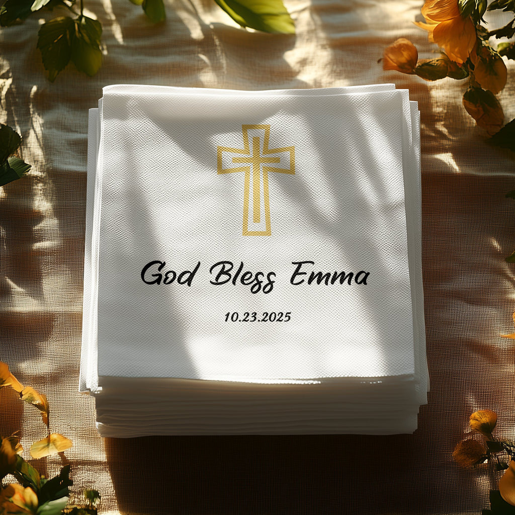 Stack of white napkins with gold cross, "God Bless Emma," and date.