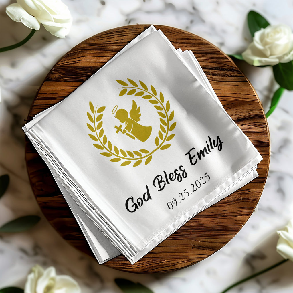 White cloth napkin with gold angel, wreath, "God Bless Emily," and date.