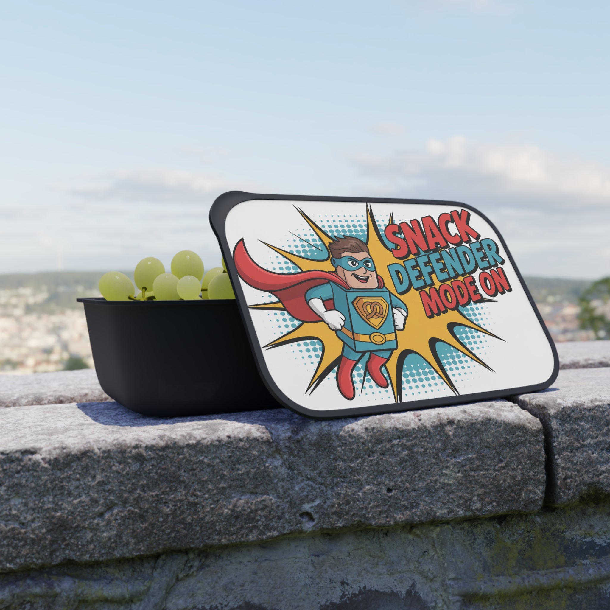 Lunchbox with superhero graphic and grapes on a stone wall.