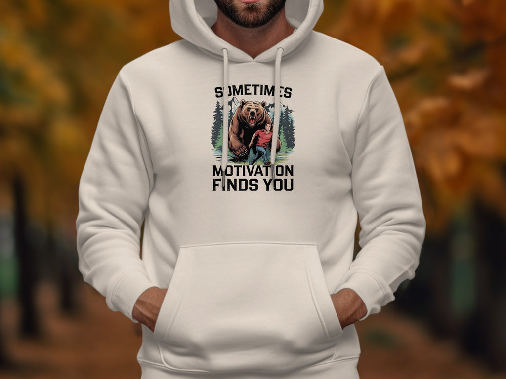 White hoodie with graphic of a person running from a bear, with text "Sometimes Motivation Finds You".