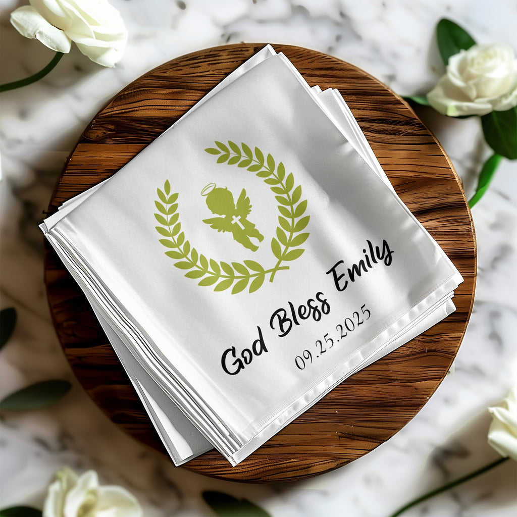 White folded napkins with green angel, wreath, "God Bless Emily", and date.