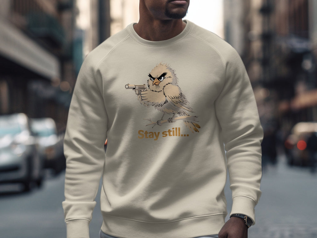 Cream sweatshirt with a cartoon bird holding a gun and text "Stay still...".