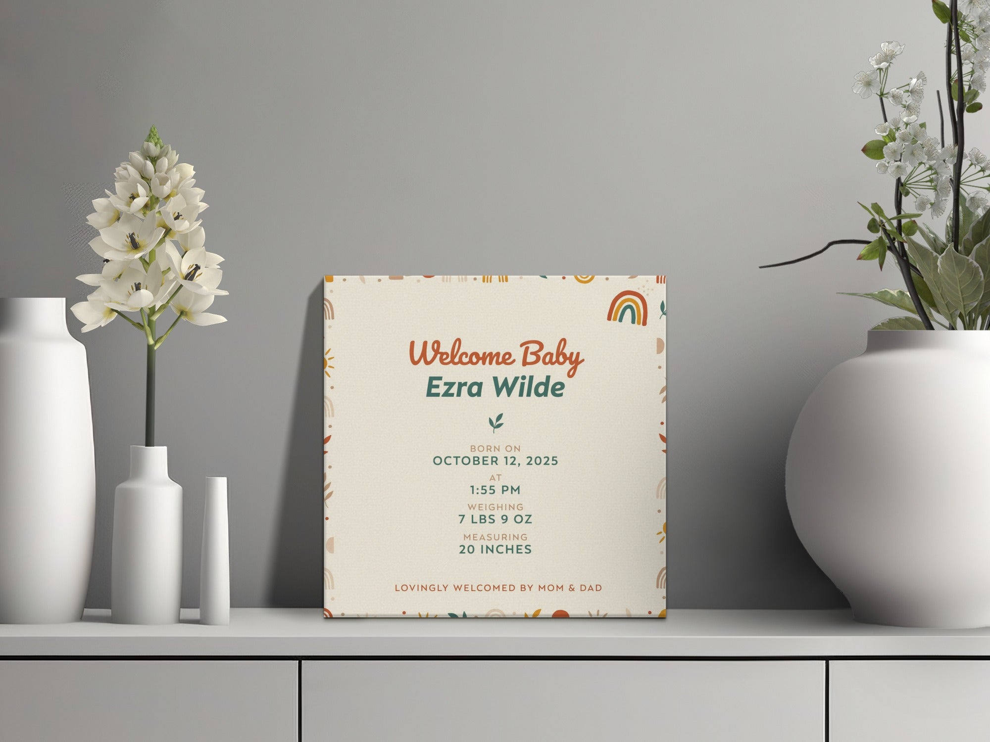 Welcome Baby Ezra Wilde sign with birth details on decorated shelf with vases and flowers.