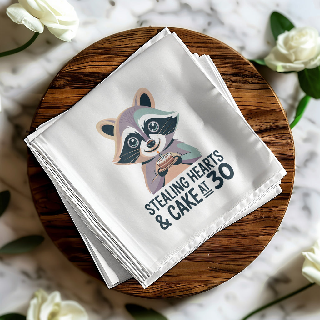 White napkin with raccoon illustration and "Stealing Hearts & Cake at 30" text.