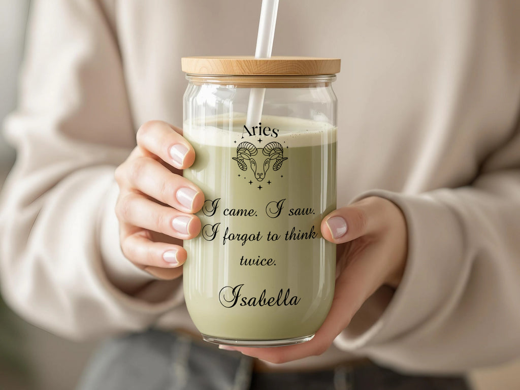 Glass tumbler with Aries zodiac sign and quote, held by hands.