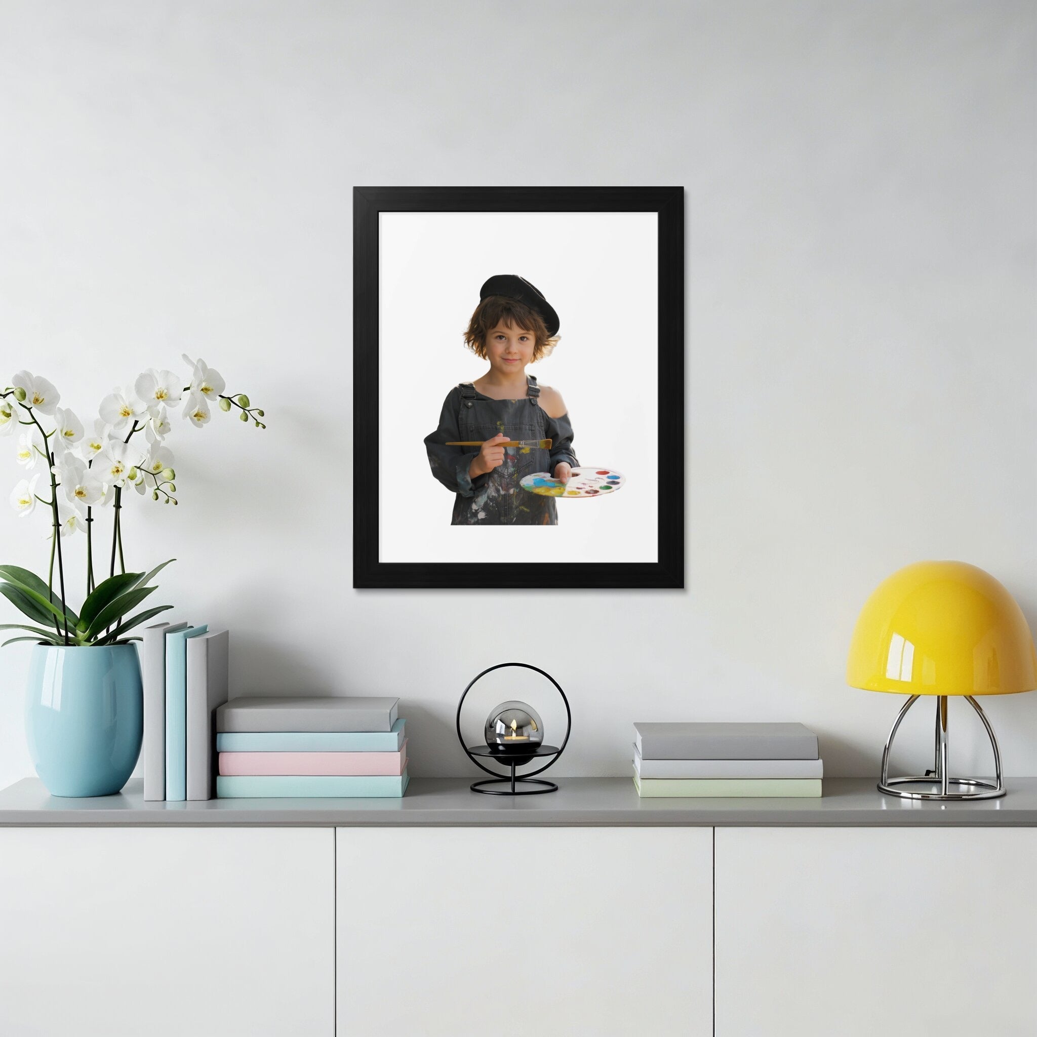 Child artist wearing overalls holds palette and paintbrush in front of a white wall.