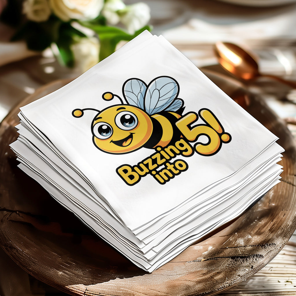 White paper napkins stacked on a wooden plate, featuring a cartoon bee and "Buzzing into 5!".