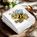 White paper napkins stacked on a wooden plate, featuring a cartoon bee and "Buzzing into 5!".